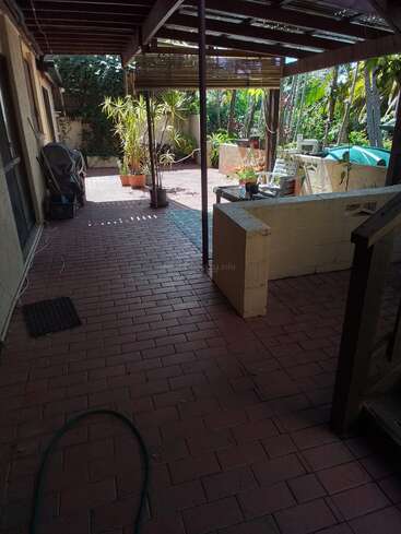 Esta imagen muestra un patio cubierto con suelo de ladrillo, muebles de exterior, plantas en macetas, una manguera de jardín, una barbacoa y una exuberante vegetación que rodea la relajante zona del jardín trasero.
