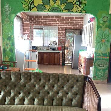 The image depicts a living room with a green couch, a cat, and a kitchen in the background, featuring a vibrant mural on the wall.