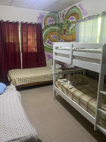 Esse quarto tem três camas, incluindo beliches, roupa de cama xadrez e com bolinhas, cortinas marrons, piso de azulejo e um grande mural de um dragão pintado na parede.