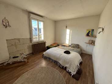 Ein gemütliches Schlafzimmer mit zwei Betten, Holzböden, einem großen Fenster und einer minimalistischen Einrichtung. Auf dem Bett liegt eine Katze und in der Nähe steht ein Schaukelpferd.