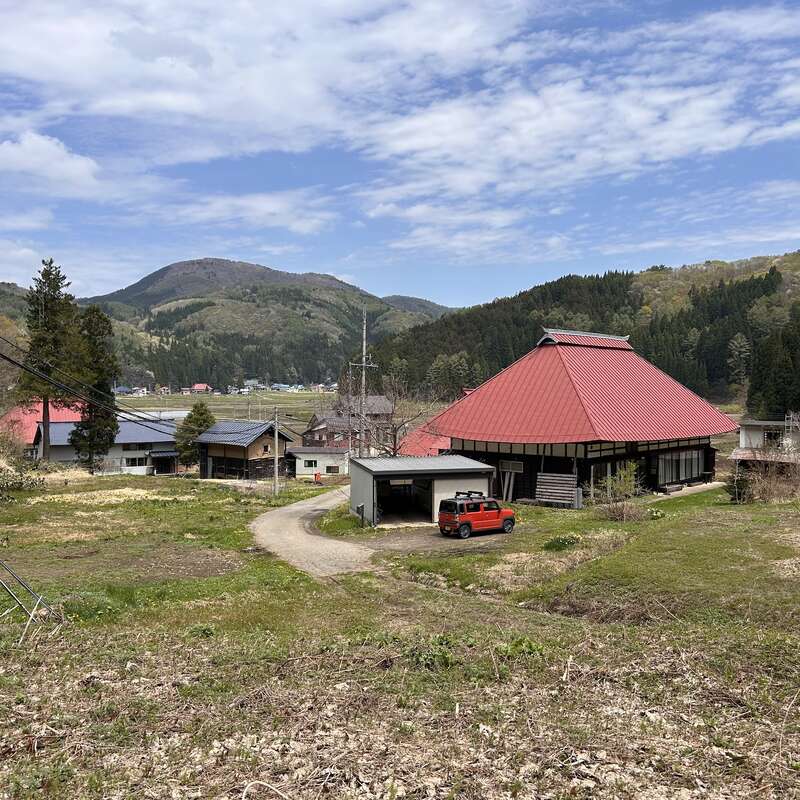 The image depicts a serene rural landscape featuring a red-roofed house, a red car, and a dirt road, set against a backdrop of rolling hills and trees.