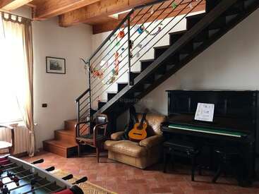A imagem mostra uma sala de estar aconchegante com uma escada, piano, mesa de pebolim e assentos confortáveis, exalando uma atmosfera calorosa e convidativa.