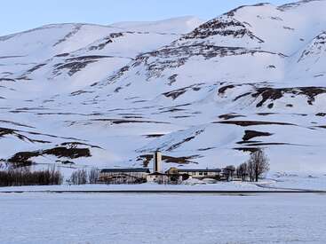 The image depicts a serene snowy landscape featuring a large building with a distinctive chimney, set against the majestic backdrop of snow-covered mountains.