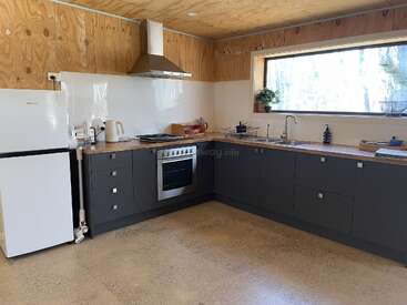 This kitchen features gray lower cabinets, wood countertops, a stainless steel oven, range hood, white refrigerator, large window, and minimalist decor with natural finishes throughout.