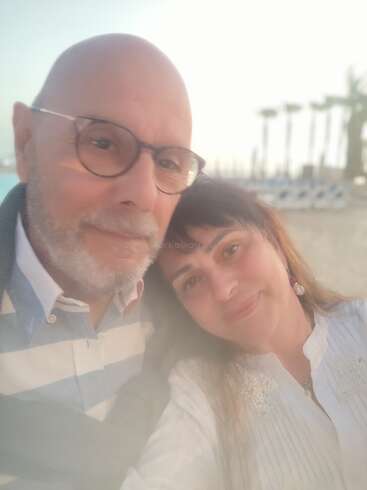 Um casal está tirando uma selfie calorosa e em close-up em uma praia ao pôr do sol. Eles parecem felizes e relaxados, com palmeiras desfocadas ao fundo.