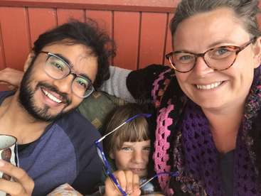 A imagem mostra uma família de três pessoas sentadas juntas, sorrindo para a câmera, com um homem à esquerda, uma criança no meio e uma mulher à direita.
