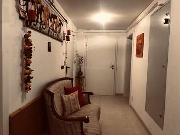 Este es un acogedor pasillo con un banco acolchado, cojines decorativos, arte mural, una guirnalda colgante, iluminación cálida y una mesita con un jarrón.