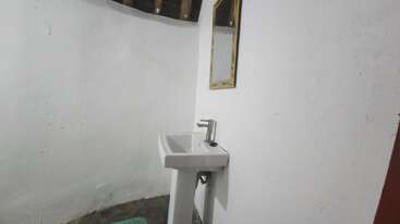 Esta imagem mostra um canto de banheiro simples com uma pia de pedestal branca, torneira moderna, um pequeno espelho retangular acima, paredes pintadas de branco e um piso de concreto. Decoração minimalista.