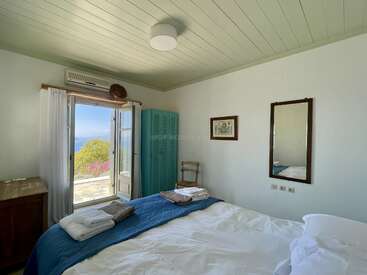 Dieses gemütliche Schlafzimmer hat ein großes Bett, gefaltete Handtücher, Holzmöbel, einen Spiegel, Meerblick durch Fenstertüren und natürliches Sonnenlicht, was eine ruhige, einladende Atmosphäre schafft.