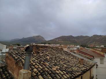 Telhados antigos de telhas de barro dominam o primeiro plano, tendo como pano de fundo montanhas distantes e um céu nublado sobre um vilarejo pitoresco. Atmosfera tranquila e pitoresca.