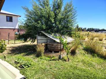 The image shows a backyard with tall grass, a tree, and a wooden barrel shelter. A house stands nearby under a clear blue sky.