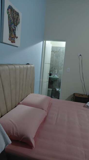 A neatly made bed with pink sheets and pillows, beige headboard, colorful elephant wall art, an open bathroom door, and some electronics plugged into the wall.