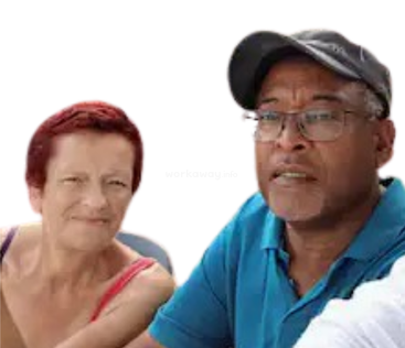 Una mujer con el pelo corto y rojo sonríe, mientras que un hombre con gafas y una gorra oscura, vestido con una camisa azul, mira hacia delante. Ambos aparecen juntos al aire libre.