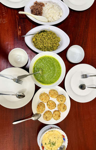 La mesa está puesta con platos, cuencos y cubiertos, y hay arroz, curry verde, judías mungo, hamburguesas vegetales y una tortilla con hierbas.