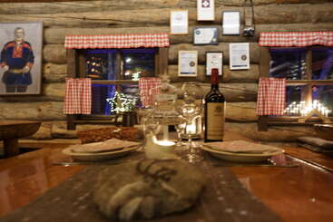 Essa aconchegante sala de jantar em cabana de madeira tem uma decoração rústica, uma mesa de jantar arrumada, vinho, luz de velas, cortinas xadrez, prêmios nas paredes e um retrato tradicional.