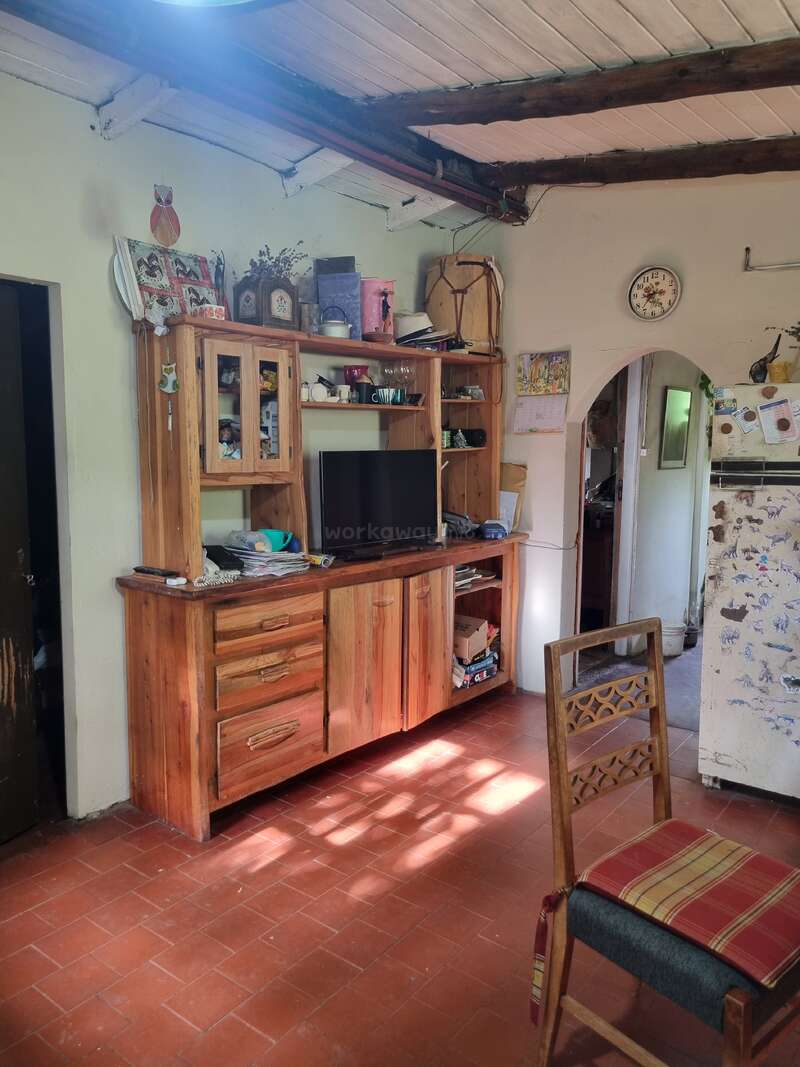 Esta acogedora habitación cuenta con muebles rústicos de madera, televisor, reloj, nevera, varios adornos, vigas vistas en el techo, suelo de baldosas rojas y una silla de madera.
