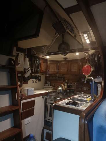 Una acogedora cocina de barco con armarios de madera, una cocina, un fregadero, utensilios colgados y una iluminación cálida, que ofrece un espacio acogedor, funcional y ordenado para cocinar a bordo.
