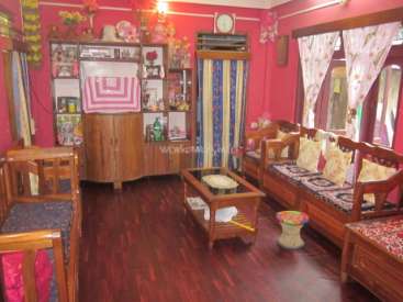 The image depicts a living room with a red wall, wooden furniture, and a window with curtains, featuring a couch, coffee table, and dining table.
