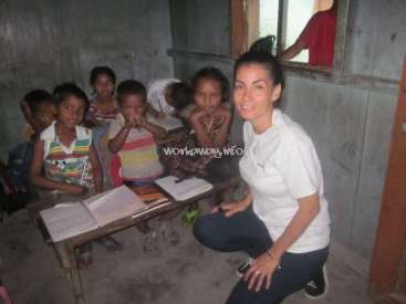 The image depicts a woman kneeling beside a group of children in a classroom, with a watermark reading "workaway.info" in the center.