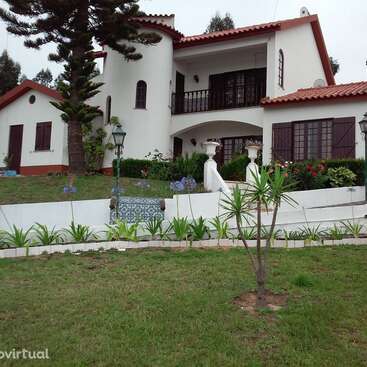 L'image représente une maison blanche avec un toit rouge et une pelouse bien entretenue, avec une clôture blanche et une variété de plantes et de fleurs dans la cour avant.