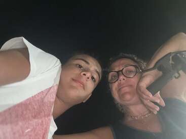 Um jovem e uma mulher mais velha estão olhando para a câmera, tirando uma selfie à noite. Eles são iluminados por uma fonte de luz abaixo.