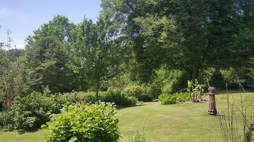 The image depicts a serene outdoor setting, featuring a well-manicured lawn with trees and bushes, evoking a sense of tranquility and natural beauty. The scene is likely a residential or park area.