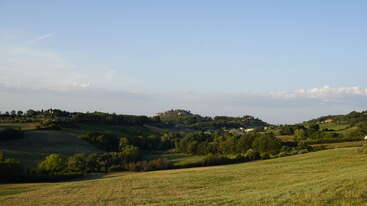 Eine friedliche Landschaft mit sanften grünen Hügeln, Bäumen, Häusern in der Ferne und einem strahlend blauen Himmel. Die Szene strahlt Frieden, natürliche Schönheit und ländliche Ruhe aus.