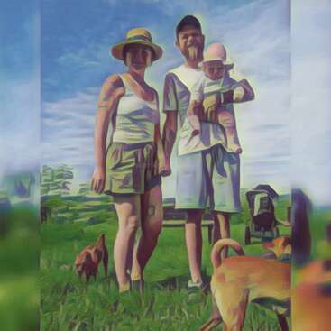 A family of three stands outdoors on green grass, accompanied by two dogs. The parents wear summer attire, and the sky is blue with scattered clouds.