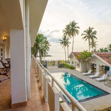 Das Bild zeigt eine ruhige tropische Umgebung mit einem Pool, Palmen und einem weißen Gebäude, mit einem ruhigen Blick auf den Ozean im Hintergrund.