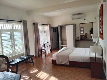 La imagen muestra un dormitorio sereno con paredes blancas, una cama grande y una ventana con las persianas abiertas, que transmite una sensación de calma y tranquilidad.