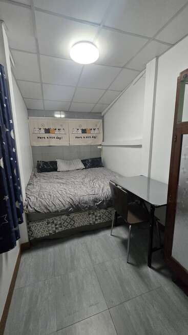 Une petite chambre confortable avec un lit, deux oreillers, une pancarte sur la table de chevet indiquant « Passez une bonne journée ! », un bureau, deux chaises et un sol carrelé.