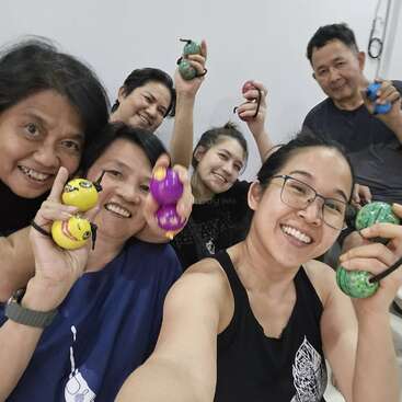 Six personnes souriantes posent ensemble pour un selfie de groupe amusant, tenant fièrement des balles anti-stress colorées et affichant un air joyeux, heureux et détendu dans un intérieur lumineux.