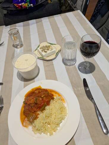 A table set for a meal featuring rice and stew, white cheese with herbs, a tub of grated cheese, water, red wine, and a decorated plate of candies.