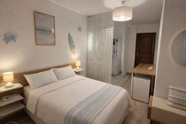 Este quarto aconchegante tem uma cama de casal, iluminação suave, decoração com tema litorâneo, um frigobar, uma mesa de madeira, paredes claras e uma divisória decorativa de vidro ao lado da cama.