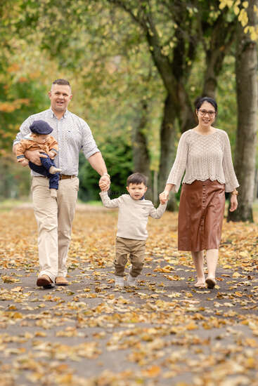 Une famille heureuse de quatre personnes se promène dans un parc couvert de feuilles d'automne. Les parents tiennent les mains de leur fils tandis que le père porte un bébé.