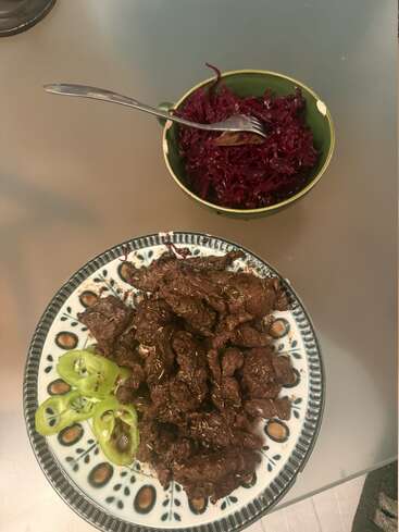 Une assiette décorative contient des lamelles de bœuf cuit assaisonné et des tranches de poivrons verts. À côté, un bol contient du chou rouge râpé et une fourchette repose à l'intérieur.