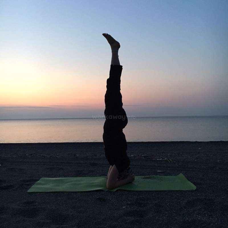 The image depicts a person performing a headstand on a green yoga mat at the beach, with the ocean and sunset visible in the background.