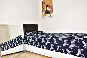 Esta imagem mostra um quarto arrumado com uma cama de solteiro com roupa de cama com estampa de zebra, um espelho grande ao lado e um retrato pendurado na parede.
