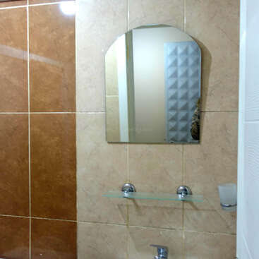 Este é um banheiro pequeno com paredes de azulejos marrons e bege, com um vaso sanitário, uma pia branca, um espelho montado, uma prateleira de vidro e um porta-sabonete.