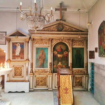Das Bild zeigt einen reich geschmückten orthodoxen christlichen Kirchenaltar mit goldenen Verzierungen, religiösen Ikonenbildern, einem großen Kreuz, Kronleuchter, Kerzen und einem Gebetspult.