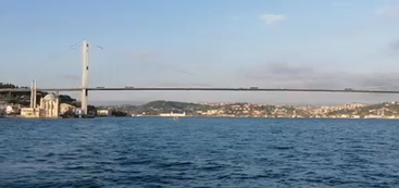 A wide bridge spans across a blue body of water, with a cityscape in the background. The sky is clear, suggesting a calm day.