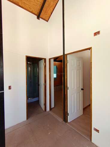 Dieses Bild zeigt einen kleinen Innenraum mit zwei weißen Türen, von denen eine zu einem Badezimmer mit Dusche, hellen Wänden und einer hohen Holzdecke führt.