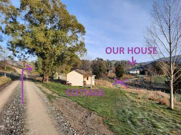 A gravel road leads past a small cottage, surrounded by greenery and trees. Purple text points out “COTTAGE” and “OUR HOUSE” in the distance.