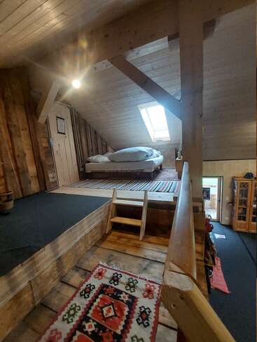 Esse quarto aconchegante no sótão tem paredes de madeira, um teto inclinado com uma claraboia, uma cama pequena, tapetes coloridos e uma escada curta que leva para cima.