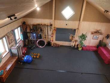 Essa espaçosa sala de madeira contém equipamentos de ginástica e circo, tambores africanos, plantas, bancos, um espelho, janelas claras, tecidos coloridos e uma atmosfera aconchegante, artística e acolhedora.