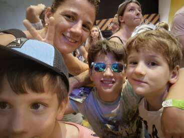 Eine Frau und drei Jungen lächeln für ein Selfie in einer überfüllten Halle. Die Atmosphäre ist lebendig und fröhlich und fängt einen lustigen gemeinsamen Moment ein.