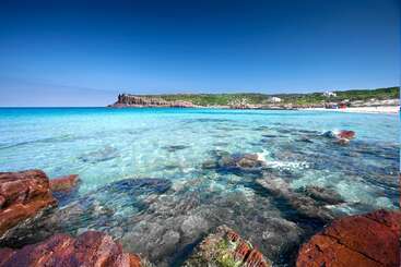 The image depicts a serene beach scene with clear blue water, a sandy shore, and a few people in the distance, evoking a sense of tranquility and relaxation.