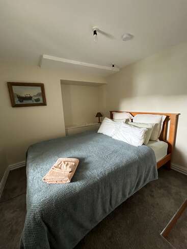 This image shows a small, cozy bedroom with a double bed covered in a textured gray blanket. A towel is neatly folded on the bed.