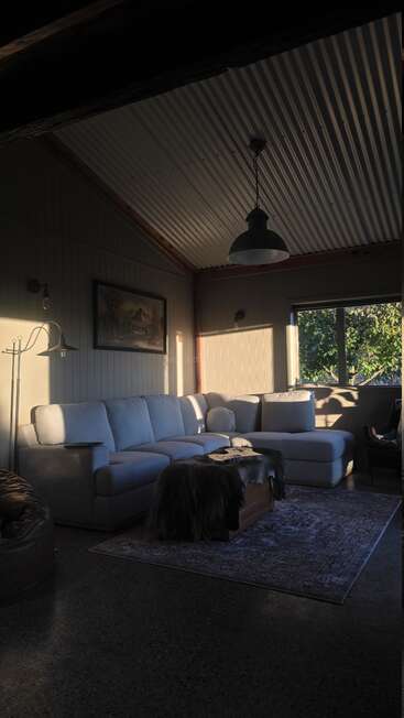 La lumière du soleil inonde un salon confortable, avec un canapé modulable, une décoration rustique, une grande fenêtre, un tapis moelleux et une atmosphère chaleureuse et accueillante. L'espace dégage une impression de sérénité et de convivialité.