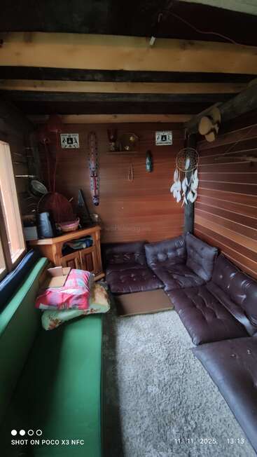 This cozy, rustic room features wooden walls, a green couch, brown sectional seating, dreamcatcher, signs, decorative items, and a small cabinet filled with various objects.